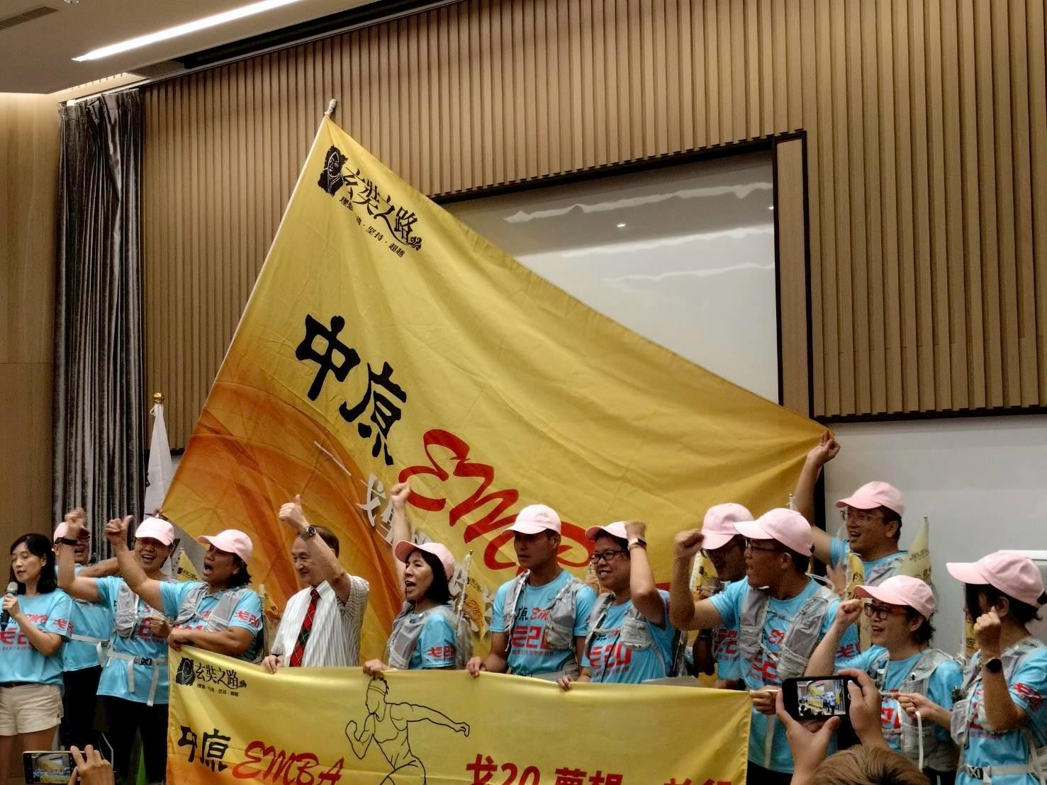 中原EMBA成員高舉隊旗，象徵群體合作與生命連結的教育實踐。