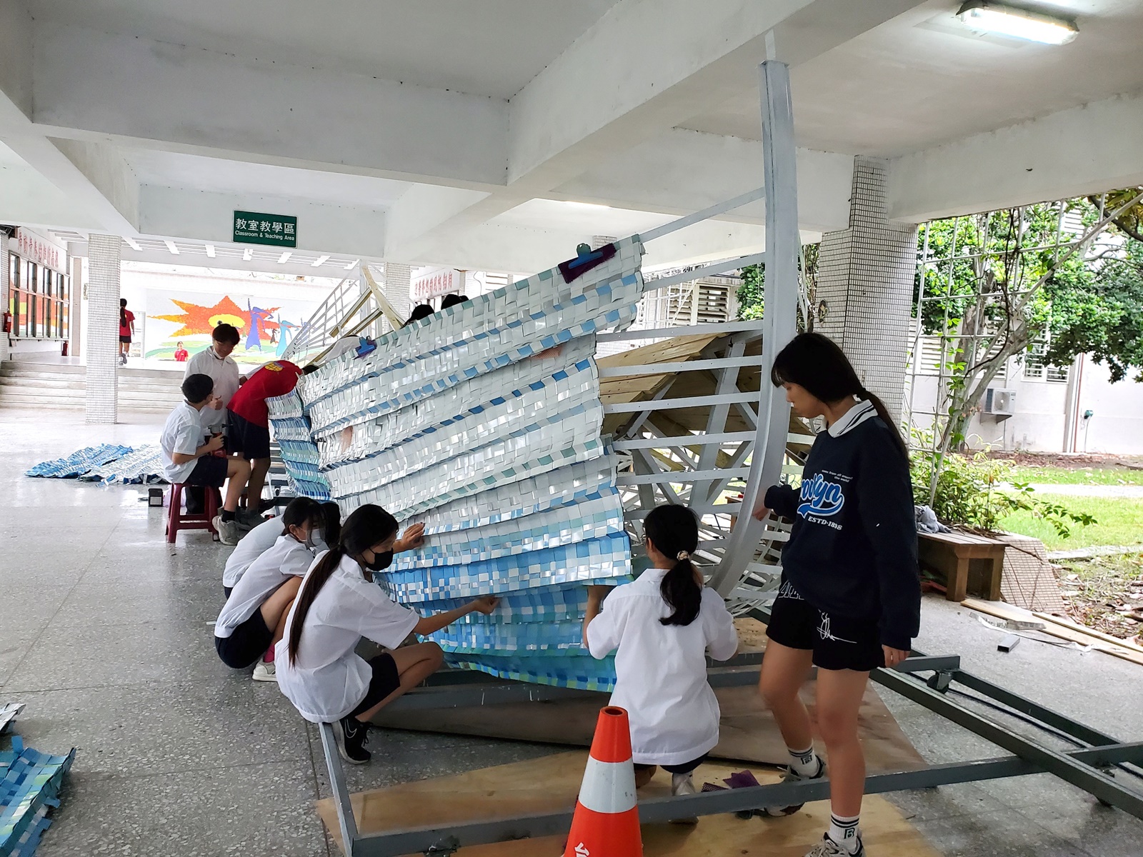 學生將編織的鋁片固定在船身骨架上，要將水平編織固定在弧形的船身上，別具挑戰