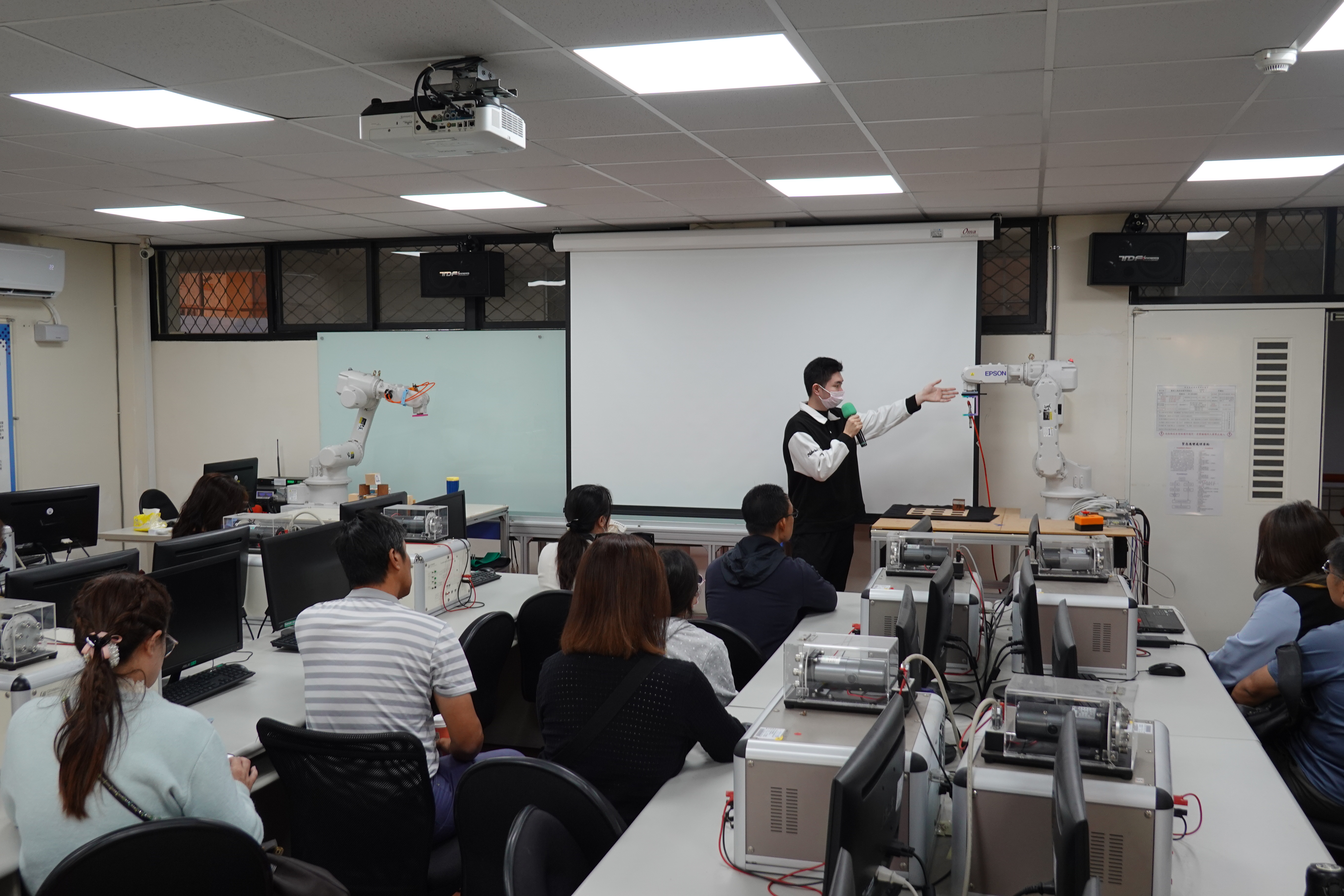 邱謙松教授團隊於機器人實驗室展示自動化教學設備，說明機器手臂操作與智慧控制研究現況。